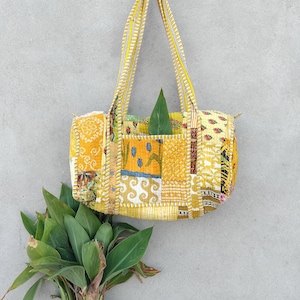 May include: A yellow patchwork tote bag with a leaf inside. The bag has a long strap and is made of quilted fabric.