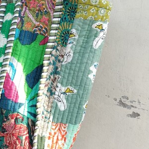 May include: A patchwork tote bag with a green, white, and orange floral pattern. The bag has a striped handle and is made of quilted fabric.