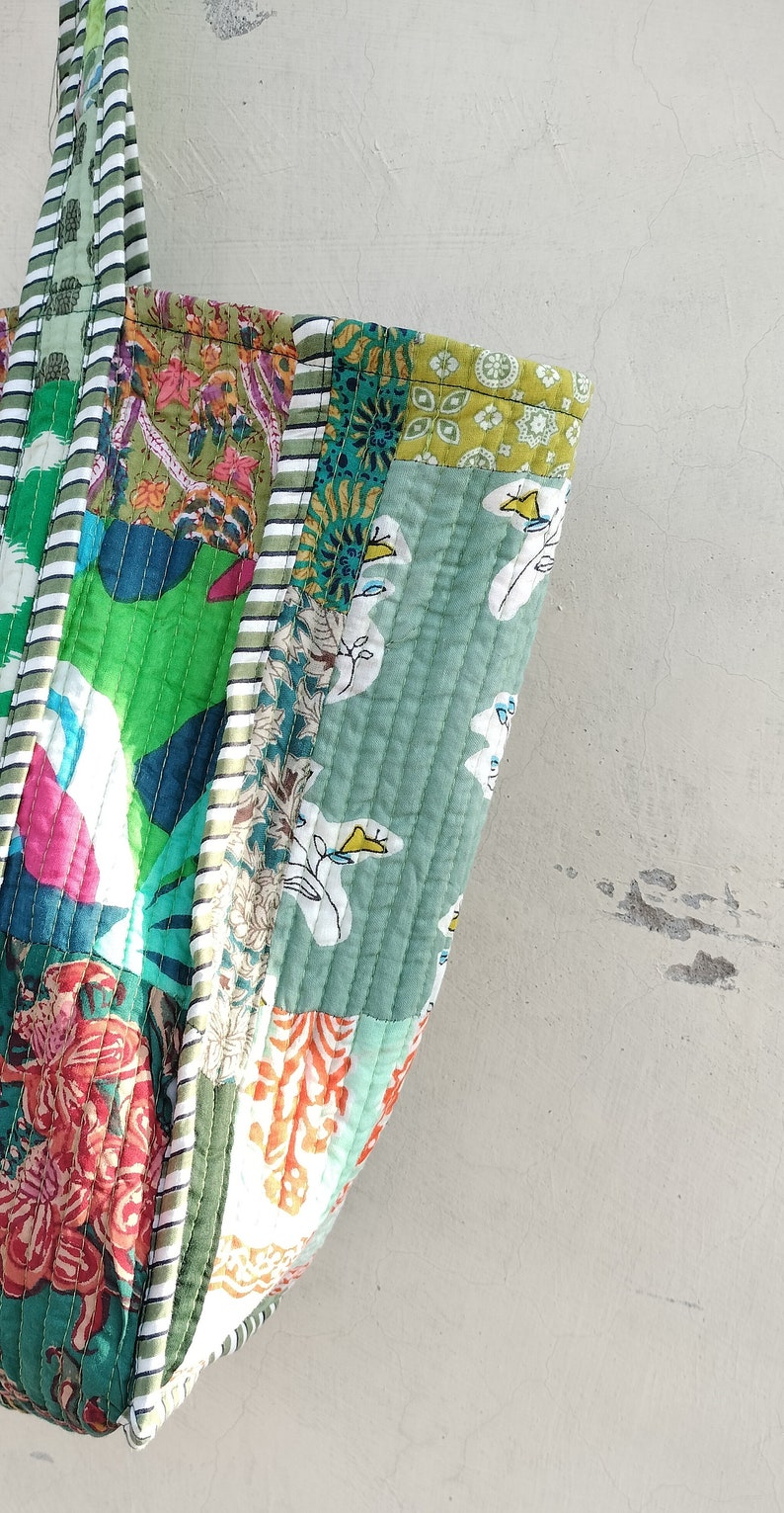May include: A patchwork tote bag with a green, white, and orange floral pattern. The bag has a striped handle and is made of quilted fabric.
