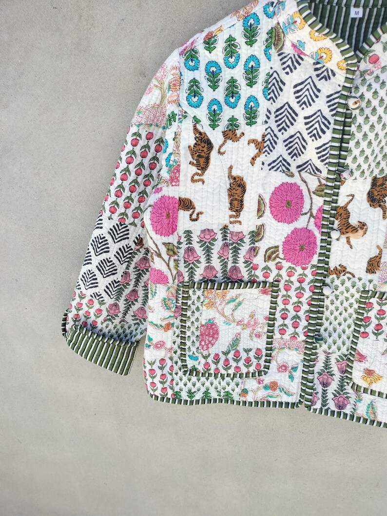 May include: A patchwork jacket with a variety of patterns and colors. The jacket features floral, tiger, and geometric designs in pink, blue, green, and white. The jacket has a green striped trim and two pockets.