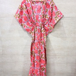 May include: A pink and red floral print kaftan with a V-neck and short sleeves. The kaftan has a drawstring waist and a long, flowing skirt.