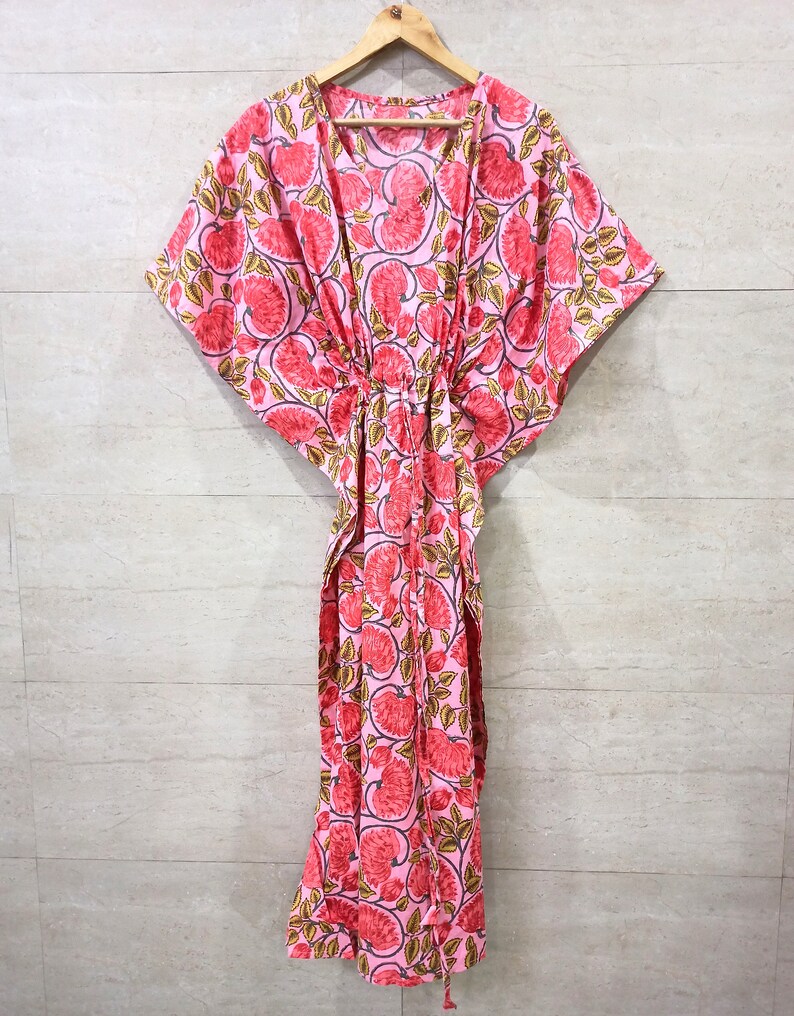 May include: A pink and red floral print kaftan with a V-neck and short sleeves. The kaftan has a drawstring waist and a long, flowing skirt.
