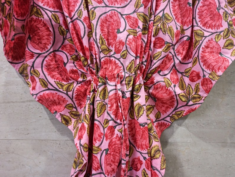 May include: Pink cotton kaftan with a floral print featuring red flowers and green leaves.