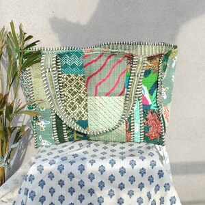 May include: A patchwork tote bag with a green, blue, and pink color scheme. The bag has a large, rectangular shape and two handles. The bag is made of fabric and has a quilted design.