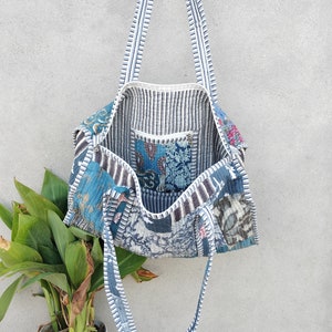 May include: A blue and white patchwork tote bag with striped straps. The bag is made of different fabrics and has a quilted design.