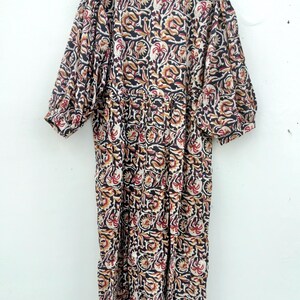 May include: A long, patterned dress with a floral design in black, red, and tan. The dress has short sleeves and is hanging on a wooden hanger against a white wall. The fabric appears to be lightweight.