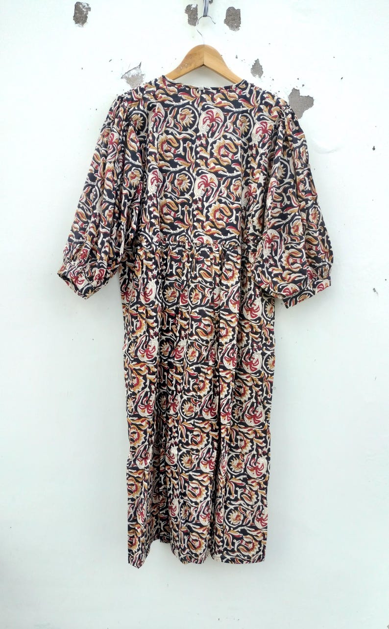 May include: A long, patterned dress with a floral design in black, red, and tan. The dress has short sleeves and is hanging on a wooden hanger against a white wall. The fabric appears to be lightweight.