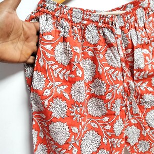 Puede incluir: Pantal&oacute;n de algod&oacute;n naranja con estampado floral blanco. El pantal&oacute;n tiene una cintura el&aacute;stica y un cord&oacute;n.