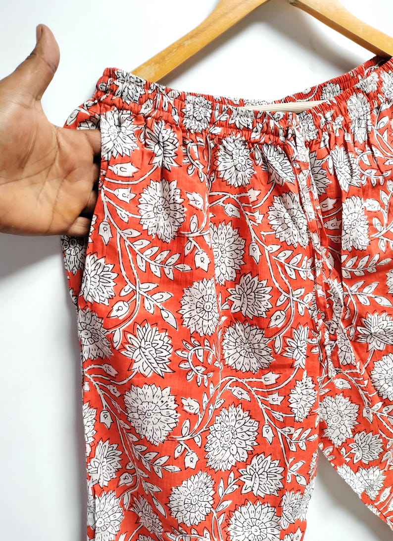Puede incluir: Pantal&oacute;n de algod&oacute;n naranja con estampado floral blanco. El pantal&oacute;n tiene una cintura el&aacute;stica y un cord&oacute;n.