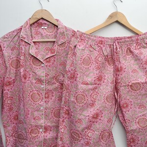 May include: Pink pajama set with a floral print. The top has a button-up front and long sleeves. The pants have an elastic waistband and a drawstring.