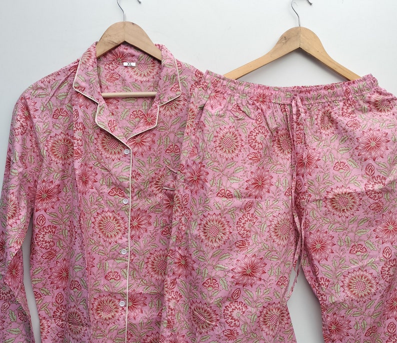 May include: Pink pajama set with a floral print. The top has a button-up front and long sleeves. The pants have an elastic waistband and a drawstring.