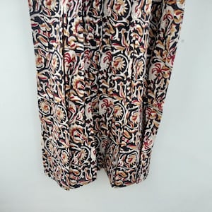 May include: Close-up of a fabric with a repeating floral pattern. The design features black, white, red, and tan colors. The fabric appears to be a lightweight material, possibly cotton or linen, with a detailed, intricate print.