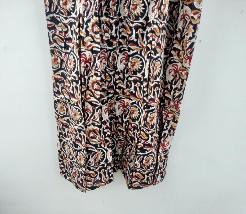May include: Close-up of a fabric with a repeating floral pattern. The design features black, white, red, and tan colors. The fabric appears to be a lightweight material, possibly cotton or linen, with a detailed, intricate print.