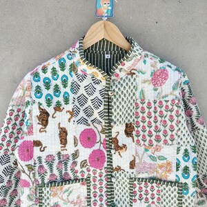 May include: A quilted jacket with a patchwork design. The jacket features various patterns, including floral, geometric, and animal prints in shades of pink, blue, green, and brown on a white background. The jacket is hanging on a wooden hanger.