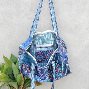 May include: A blue and white patchwork tote bag with a zippered pocket on the inside. The bag has a long strap and is made of a quilted fabric.