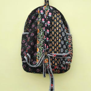 Peut inclure: Un sac à dos matelassé noir avec un imprimé floral. Le sac à dos a une fermeture à cordon et une petite poche sur le devant.