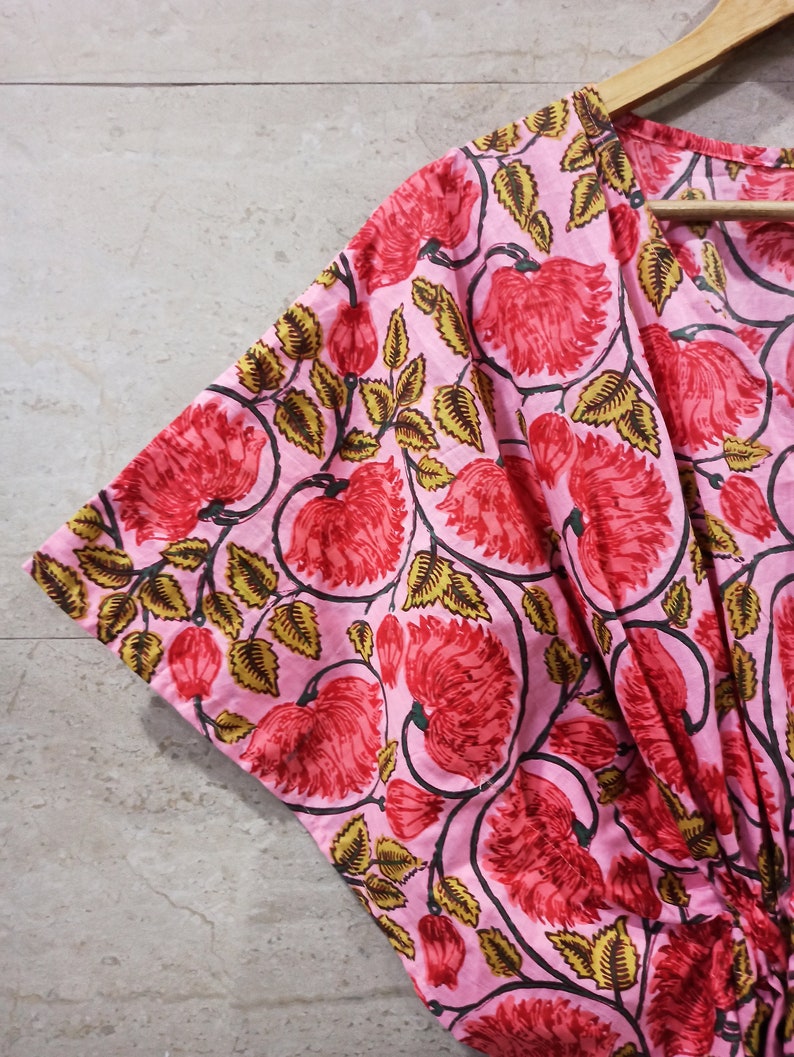 May include: Pink cotton kimono with a floral print featuring red flowers and green leaves.