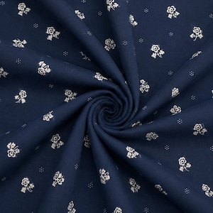 Könnte beinhalten: Ein dunkelblauer Stoff mit einem sich wiederholenden Muster aus kleinen weißen Blumenclustern und winzigen weißen Punkten. Das Material ist in einer zentralen Spirale gerafft, wodurch weiche Falten und Schatten die Textur hervorheben.