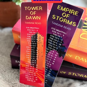 以下が含まれることがあります： タンデム読書ガイド付きの両面ブックマーク。「Tower of Dawn」は赤とオレンジのグラデーション、「Empire of Storms」は紫のグラデーション。どちらも章のペアをリストしています。