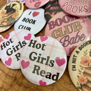 Pode incluir: Uma coleção de botões redondos e coloridos com várias frases e gráficos relacionados a livros. Os botões apresentam textos como "Hot Girls Read", "Book Club Babe" e "I Love Book Club". A paleta de cores inclui rosa, branco e preto.