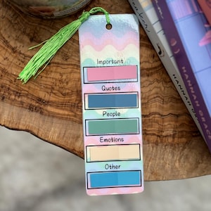 Könnte beinhalten: Ein farbenfrohes Lesezeichen mit einem Regenbogenhintergrund und einem grünen Quasten. Das Lesezeichen hat fünf Abschnitte mit den Wörtern "Wichtig", "Zitate", "Menschen", "Emotionen" und "Sonstiges" darauf.