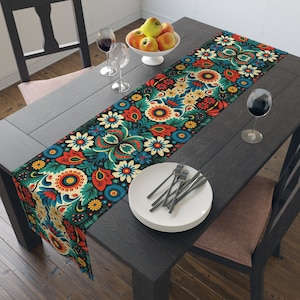 Könnte beinhalten: Ein farbenfroher Blumentischläufer mit dunkelblauem Hintergrund, verziert mit roten, gelben und grünen Blumen. Der Läufer liegt auf einem dunklen Holztisch mit einem weißen Teller und Besteck.