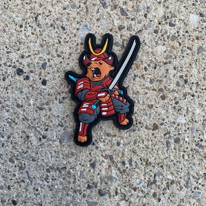 Könnte beinhalten: Ein roter und schwarzer Cartoon-Samurai-Krieger mit einem gelben Helm und einem Schwert. Der Krieger ist ein Stier mit einem grimmigen Ausdruck.