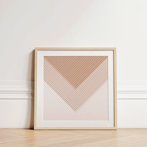 May include: Framed abstract art print featuring a geometric design. The artwork showcases a pattern of diagonal lines in shades of brown and pink, creating a layered, chevron-like composition. The print is encased in a light-colored wooden frame.