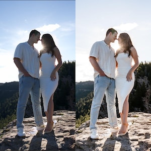 May include: A couple stands close together on a rocky cliff, silhouetted by the sun. The woman wears a white, strapless dress and the man wears a light-colored shirt and jeans. The background features a forest and a blue sky.
