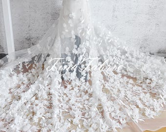 May include: White floral lace fabric with 3D flowers. The lace is delicate and intricate, with a soft, flowing texture. The fabric is perfect for creating wedding dresses, evening gowns, and other special occasion garments.