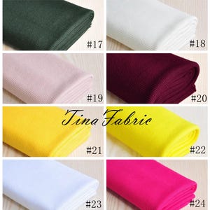 May include: A collection of ten fabric swatches in various colours, including green, white, pink, burgundy, yellow, and pink. Each swatch is rolled up and labelled with a number from 17 to 24.