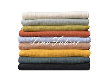 May include: A stack of ten fabric swatches in various colors, including white, light blue, yellow, orange, and brown. The swatches are folded and stacked on top of each other. The text "Tina Fabrie" is visible on the stack of fabric swatches.