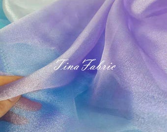 May include: A gradient ombre fabric in shades of white, light blue, purple, and lavender. The fabric is sheer and has a slight shimmer. The text "Tina Fabric" is visible in the center of the image.