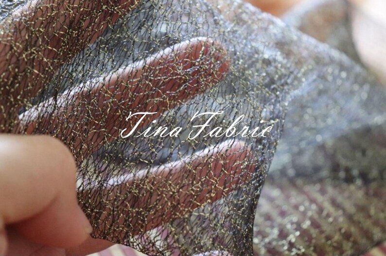 Puede incluir: Tela de malla negra con hilos met&aacute;licos dorados tejidos en toda la tela. La tela es transl&uacute;cida y tiene una apariencia delicada, casi como una telara&ntilde;a. El texto "Tina Fabric" es visible en la imagen.