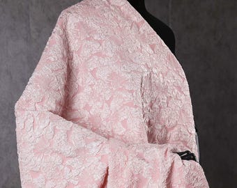 May include: A pink fabric with a white floral embossed pattern. The fabric is draped over a mannequin.