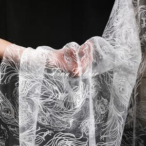 May include: White sheer fabric with a peacock feather pattern. The fabric is delicate and translucent, with a subtle shimmer.