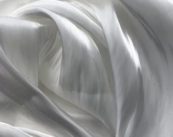 May include: Close-up of white fabric with soft folds and subtle shadows. The fabric appears to be lightweight and flowing, with a slight sheen. The overall effect is one of elegance and delicacy.