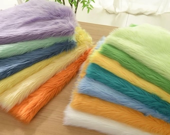 May include: Stacks of colorful faux fur fabric in shades of purple, green, blue, yellow, orange, and white. The plush material has long, soft fibers, ideal for crafts or decor.