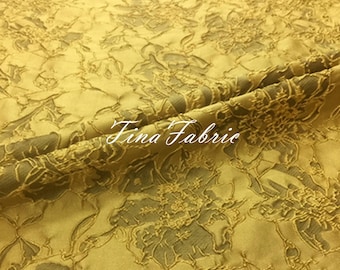 May include: A close-up of a gold fabric with a raised floral pattern. The fabric has a subtle sheen and a soft texture.