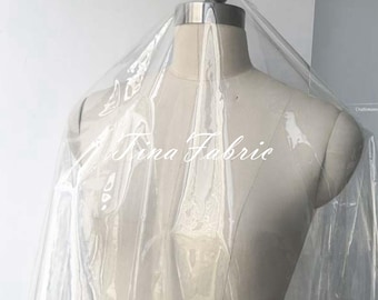 May include: Clear plastic fabric draped over a dress form. The fabric is translucent and has a slight sheen. The fabric is labeled "Rina Fabric".
