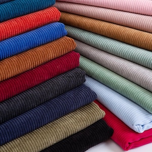 Może przedstawiać: Stos różnych kolorowych tkanin z dzianiny typu „kord”. Tkaniny są ułożone w tęczowym wzorze, z kolorami od ciemnoniebieskiego do jasnoróżowego. Wszystkie tkaniny są żebrowane i mają miękką, pluszową fakturę.