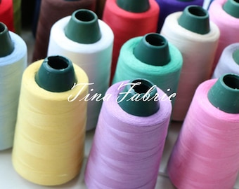 May include: A variety of spools of thread in different colors, including yellow, pink, green, white, and red. The spools are arranged in a semi-circle on a white surface. The text "Tina Fabric" is visible in the center of the image.