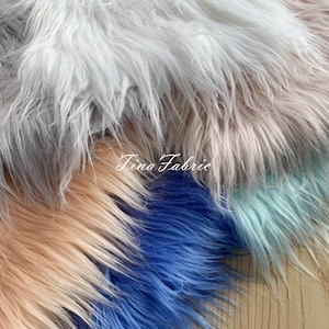 May include: Four different colors of faux fur fabric. The colors are white, light pink, blue, and light green. The fabric is soft and fluffy.