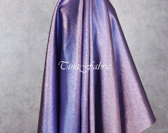 May include: A draped fabric in shades of purple and blue with a shimmering, iridescent finish. The fabric is gathered at the top, creating folds and shadows that highlight its texture. The text "Tina Fabric" is visible in the lower center.