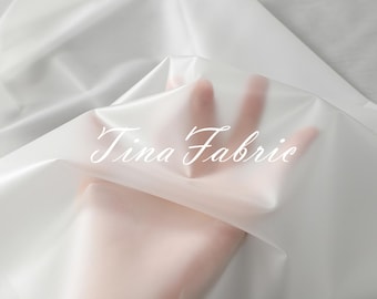 May include: A close-up of sheer white fabric, folded and draped. The fabric is translucent and has a smooth, silky texture. The text "Tina Fabric" is printed on the fabric.