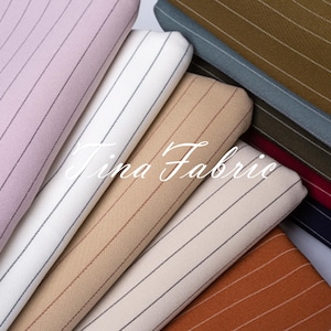Puede incluir: Una colección de muestras de tela a rayas en varios colores, incluyendo rosa, blanco, beige y naranja. La tela tiene un sutil patrón de rayas finas. El texto "Tina Fabric" es visible en el centro de la imagen.