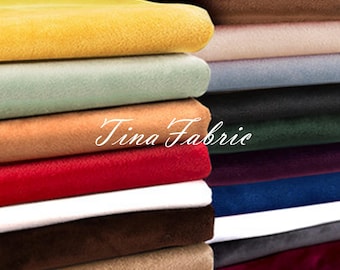 May include: A stack of fabric swatches in various colors, including yellow, green, red, brown, blue, and gray. The fabric is velvet and has a soft, plush texture. The text "Tina Fabric" is visible on the fabric.