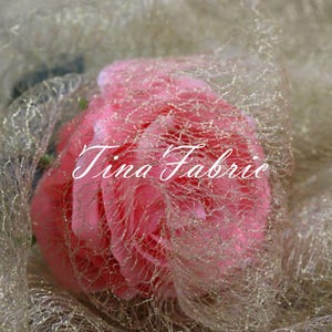 Puede incluir: Una rosa rosa envuelta en una tela de tul dorada con purpurina. La tela tiene una textura delicada y de red. El texto "Tina Fabric" es visible en la rosa.