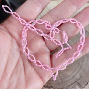 May include: A pink heart-shaped crocheted lace doily with a floral design in the center.