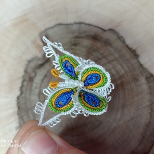 May include: A white crocheted butterfly with blue, green, and yellow accents. The butterfly has a pearl bead in the center.